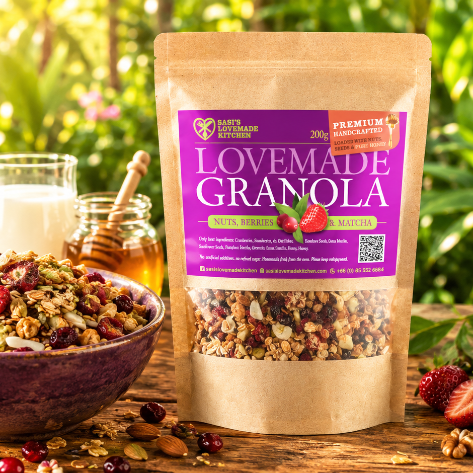 A 200 g stand-up pouch of Sasi's Lovemade Kitchen Granola sits on a wooden table outdoors, with a bowl of granola, a glass of milk, and a honey dipper in a blurred garden background. The package has a kraft paper finish with a large purple label and a clear window showing the granola inside.