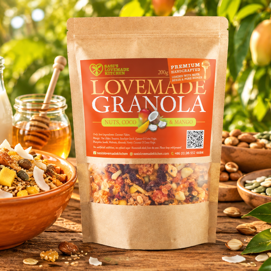 A stand-up pouch of Sasi's Lovemade Kitchen 200 g Granola, Nuts, Cocoa & Mango, displayed on a rustic wooden table surrounded by bowls of the granola, almonds, and a jar of honey in a lush, green outdoor setting.